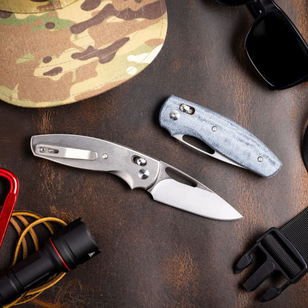 TRM Bulldog Rev B Titanium and Denim knives in a outdoorsy flat lay on brown worn leather
