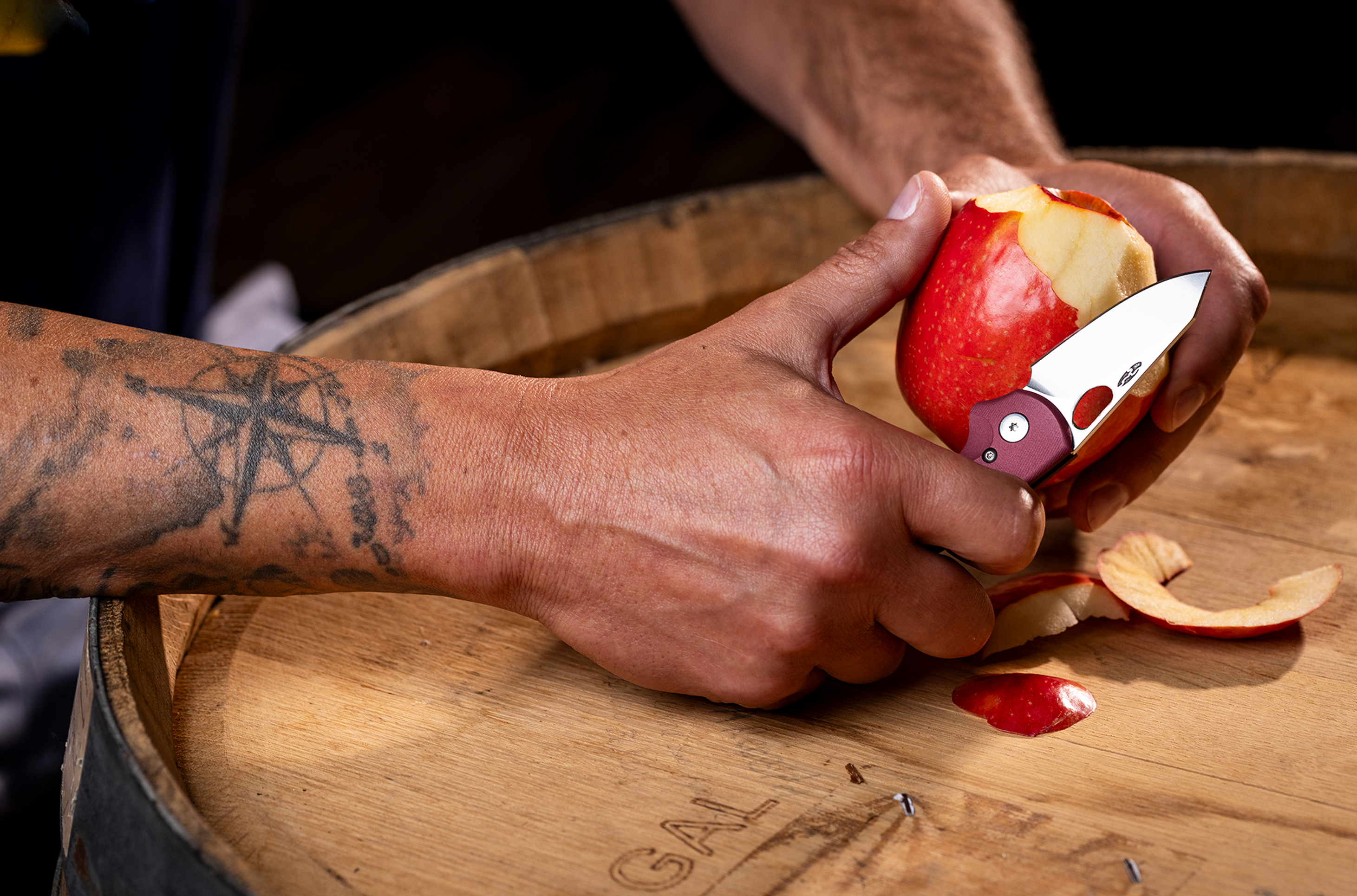 Person cutting an apple with a pocket knife on a wooden surface